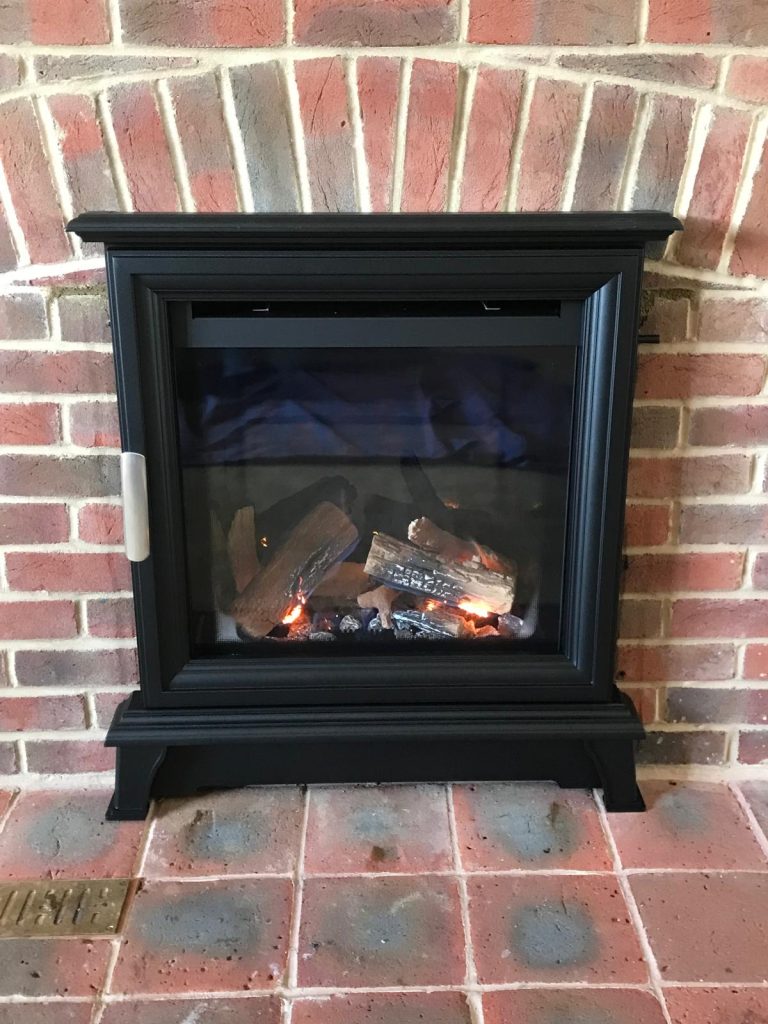 Log-effect gas stove in an exposed brick fireplace, installed by Fire Flair Direct