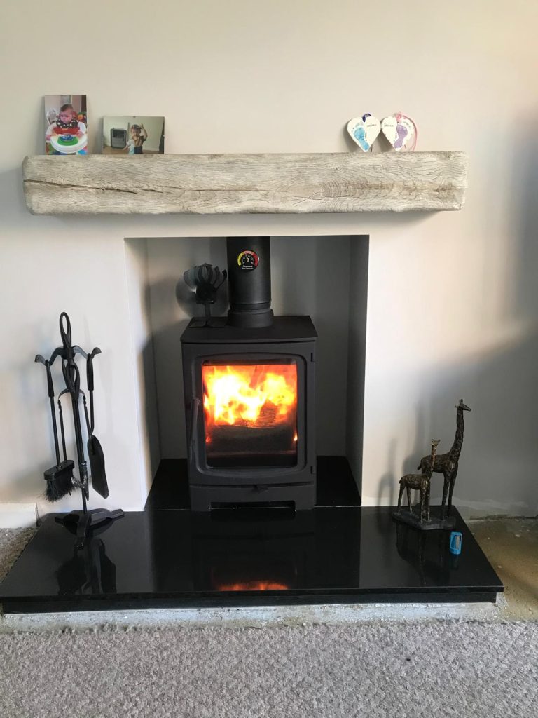 Wood-burning stove with stone beam and black granite hearth, installed by Fire Flair Direct