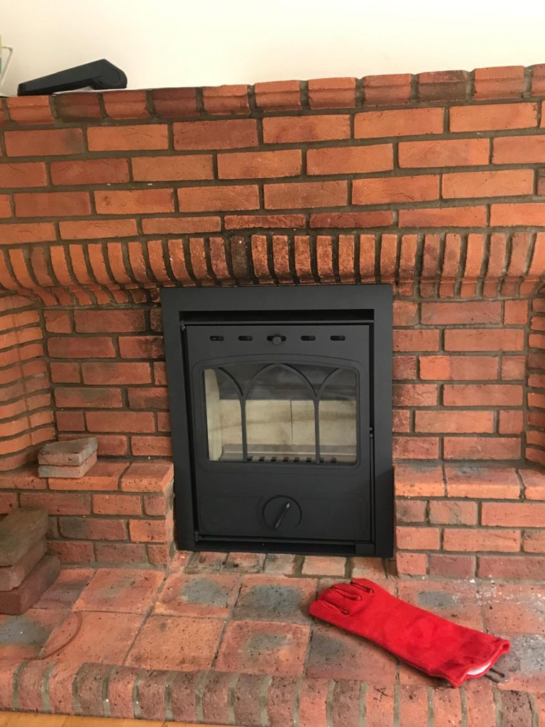 Inset wood-burning stove in a red brick fireplace, installed by Fire Flair Direct