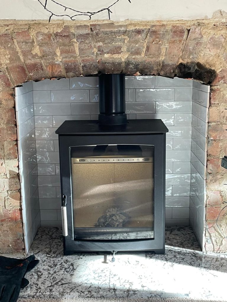 Wood-burning stove in a brick fireplace with tiled back panel, installed by Fire Flair Direct